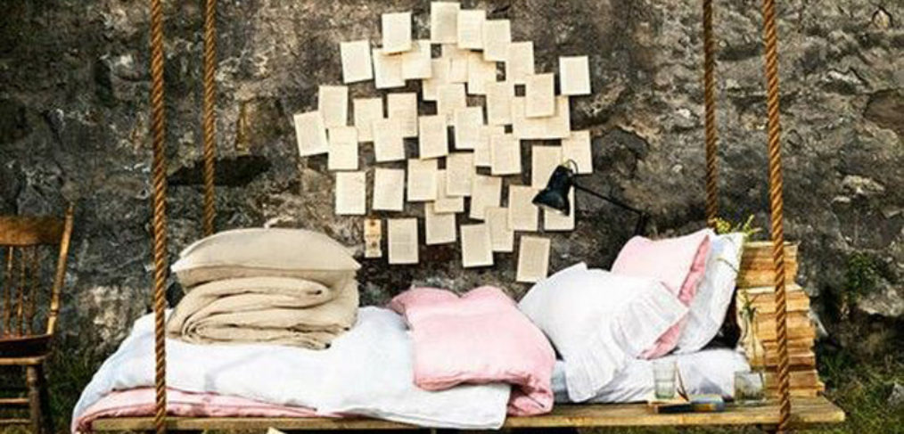 letto-altalena in legno, con coperte e cuscini, grosse corde per sostenerla e ambientazione outdoor