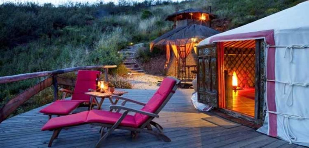 Capanne il legno per il campeggio di lusso con terrazzo esterno a doghe in legno arredato con sdraio dai cuscini fucsia e tavolino